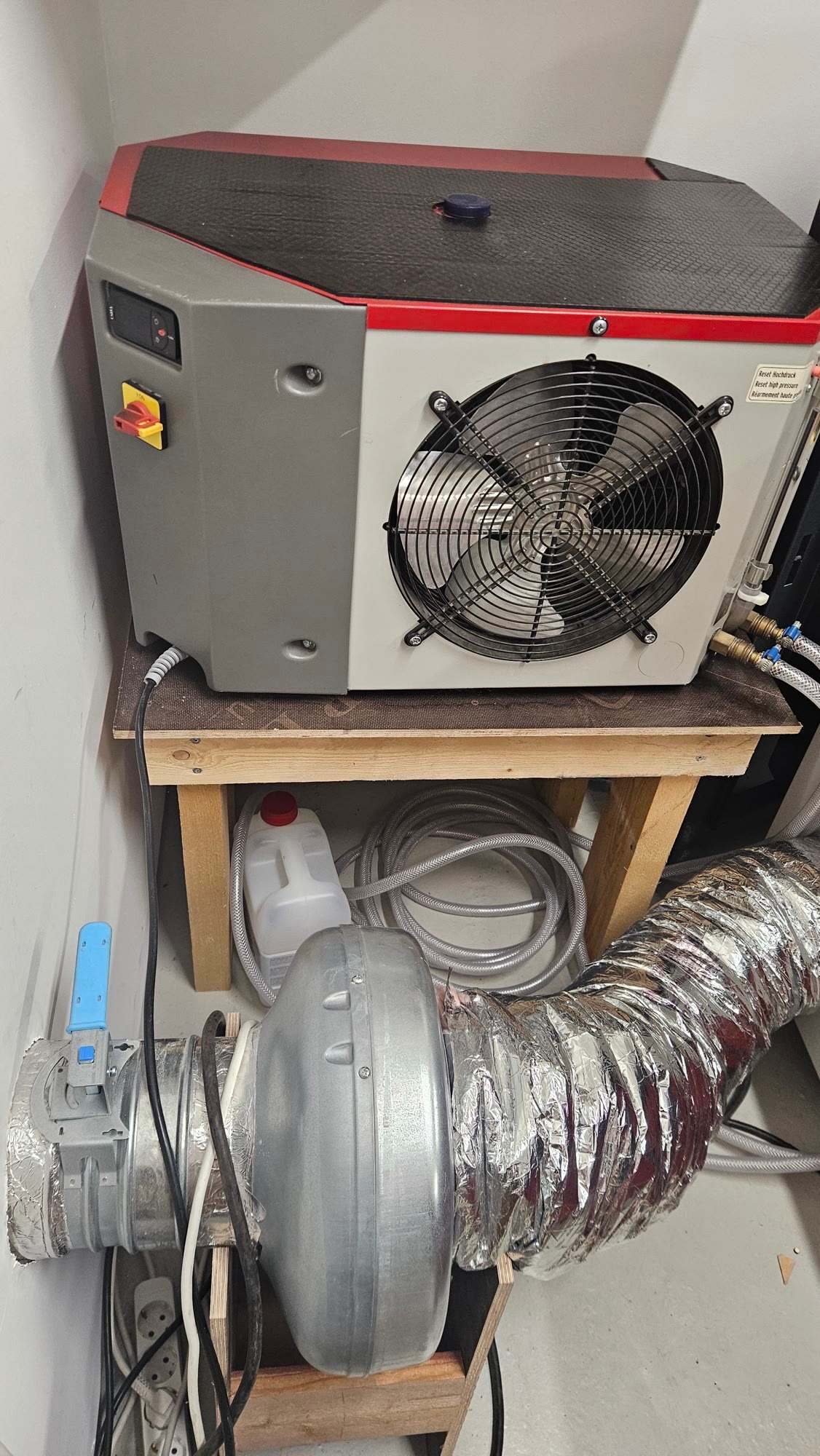 Water chiller with a large cooling fan on a wooden stand, with an exhaust blower and foil duct below