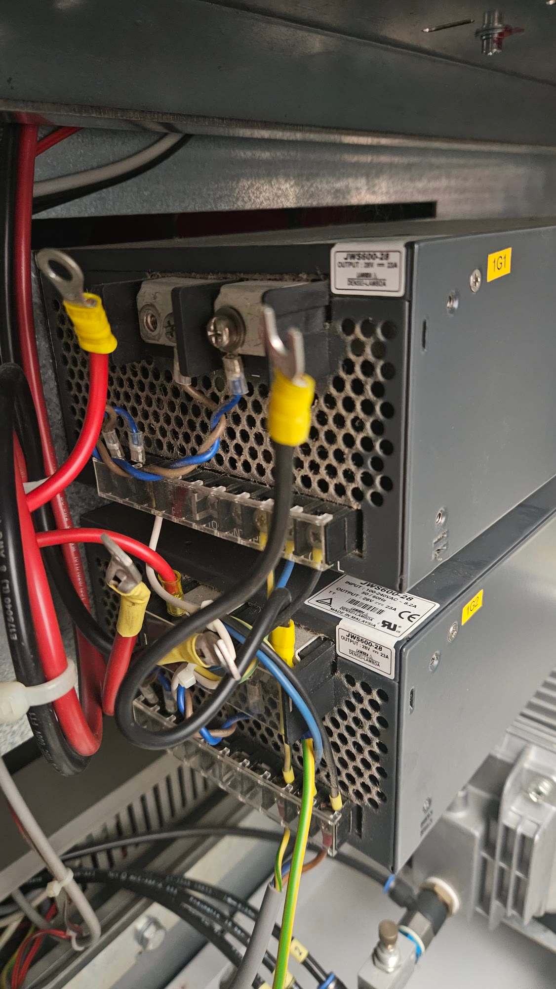 Two stacked Densei-Lambda JWS600-28 power supplies labelled 1G1 and 1G2, with red and black output cables