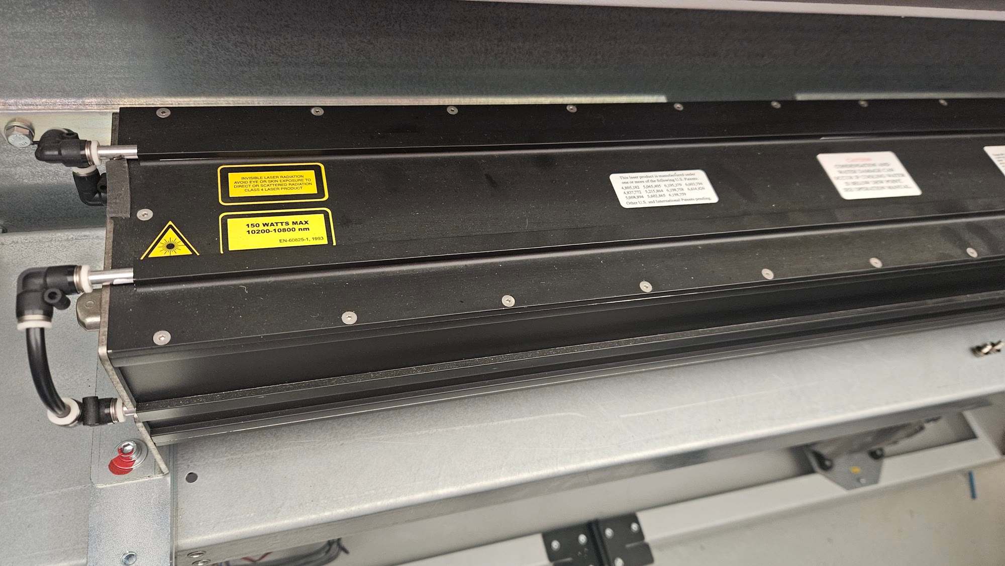 Long black Synrad laser tube with yellow warning labels and water cooling connections