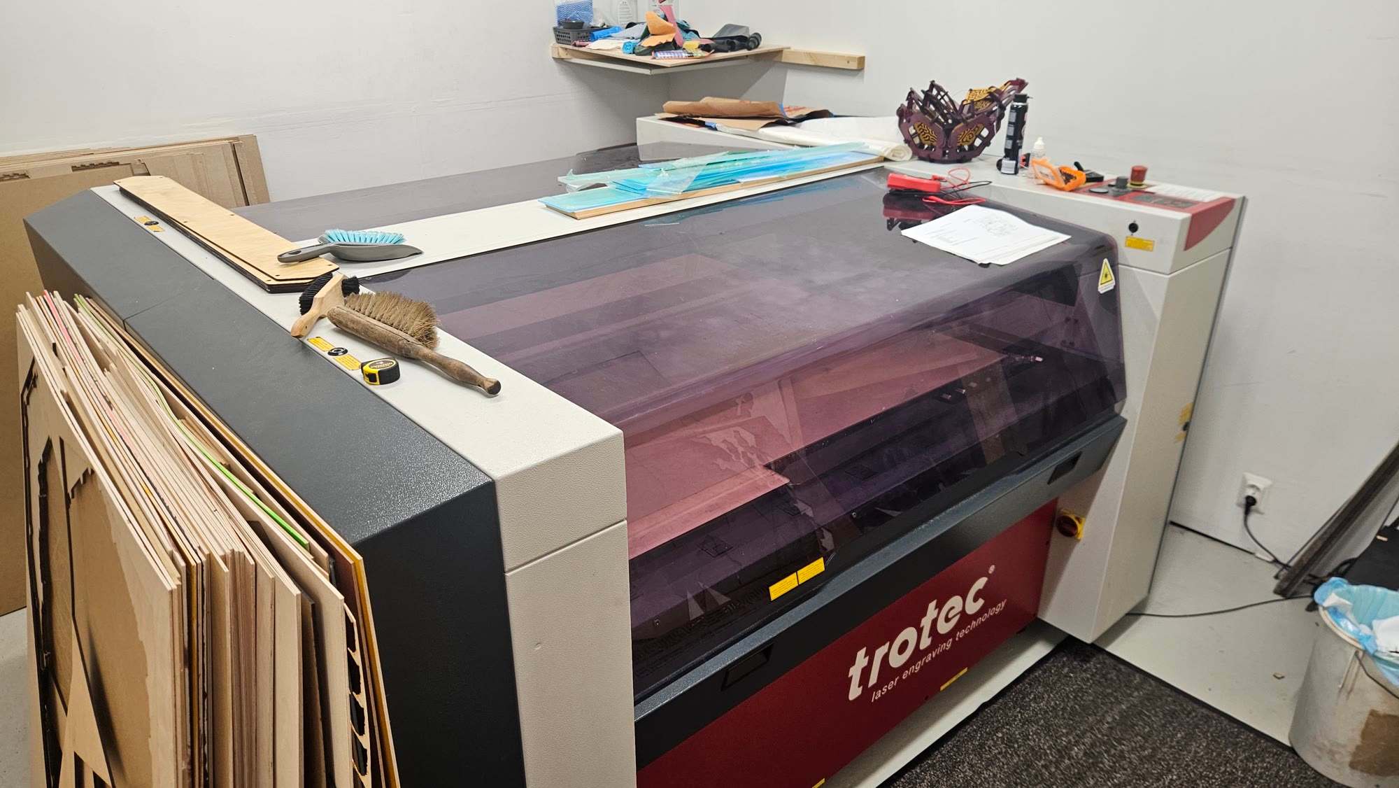 Trotec TP1313 laser cutter with a smoked purple lid, in the studio with plywood sheets leaning against it